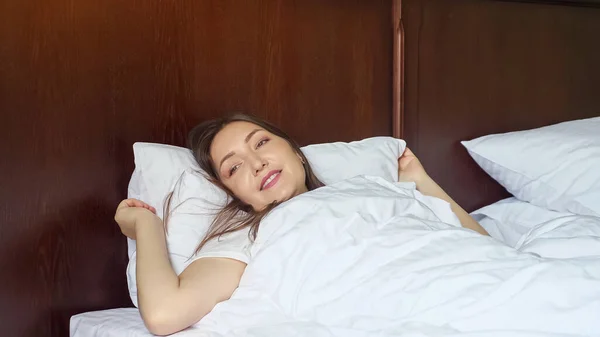 Молода жінка прокидається і розтягується, лежачи в ліжку — стокове фото