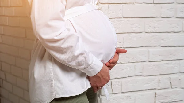 Femme enceinte coups ventre debout près du mur de briques — Photo