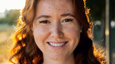 Parkta kıvırcık bakır saçlı ve çilli genç bir kadın.