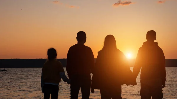 Silueta rodinných postav a drží se za ruce proti řece a západu slunce — Stock fotografie