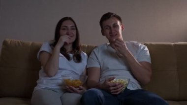 Patlamış mısırlı adam ve patates kızartmalı kadın TV izlerken gülüyorlar.