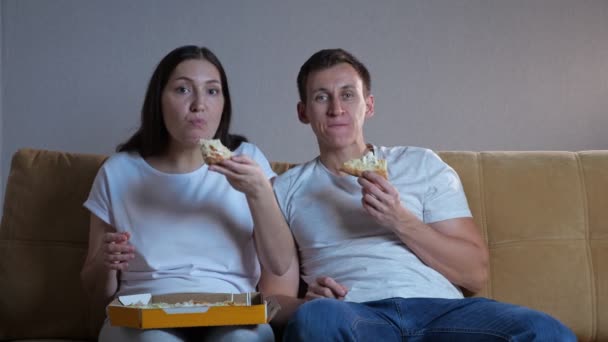 Mann und Frau essen Pizza vor dem Fernseher auf Sofa neben Katze — Stockvideo