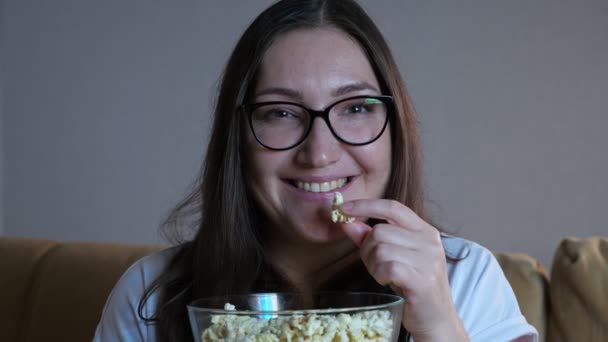 Kvinna i glasögon äter popcorn och tittar på tv — Stockvideo