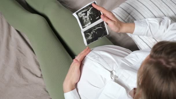 La signora incinta guarda l'immagine ecografica e accarezza la pancia — Video Stock