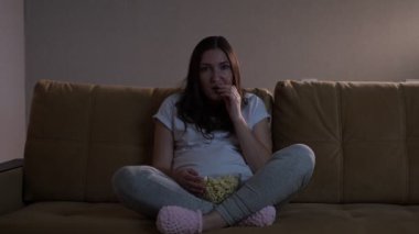 Bayan patlamış mısır yiyor ve TV 'de yarışmayı izlemekten zevk alıyor.
