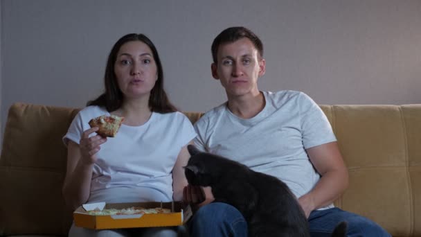 Señora se sienta por hombre en sofá come pizza alimentación marido y gato — Vídeo de stock