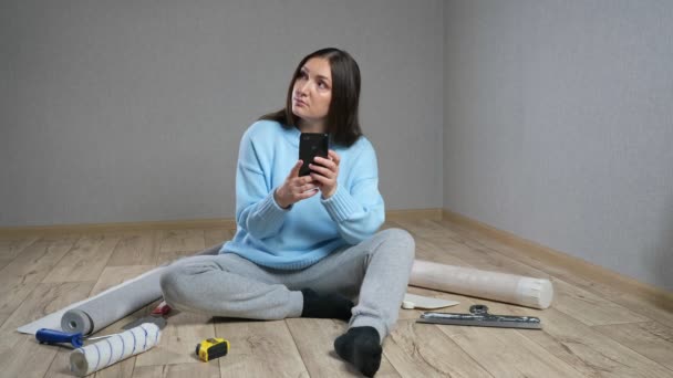 女性は床に座って家具や部屋の装飾を選択します — ストック動画