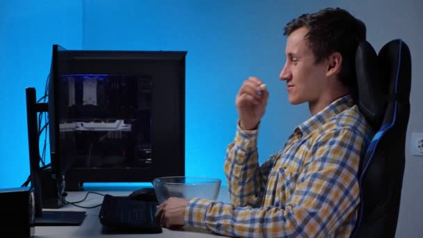 Молодой человек смотрит поток с компьютером и ест попкорн — стоковое видео