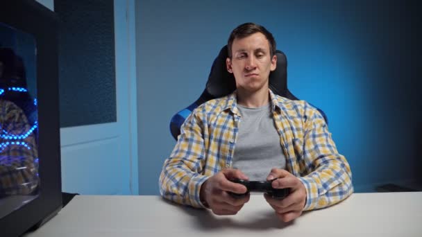 Jeune homme joue à un jeu d'ordinateur avec manette de jeu dans une pièce semi-sombre — Video