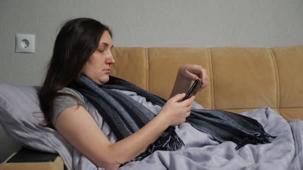 Больная женщина сидит на диване и заказывает лекарства через смартфон — стоковое видео