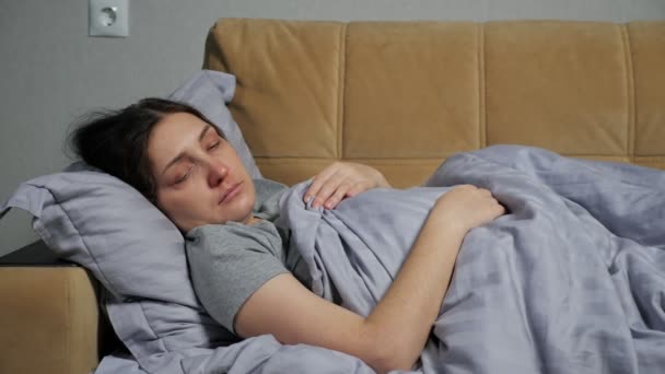 Больной молодой женщины лежит на диване под одеялом и кашляет — стоковое видео