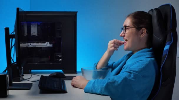 Mujer joven observa corriente con computadora y come palomitas de maíz — Vídeo de stock