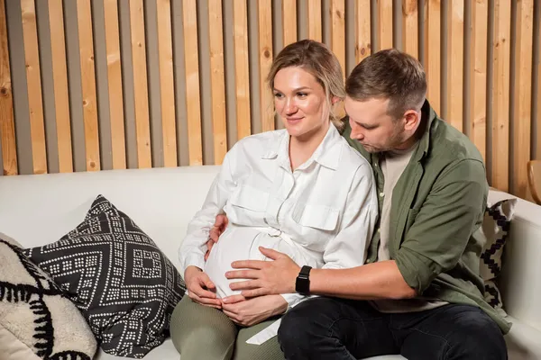 Homme câlins femme enceinte assis sur le canapé confortable dans le salon — Photo