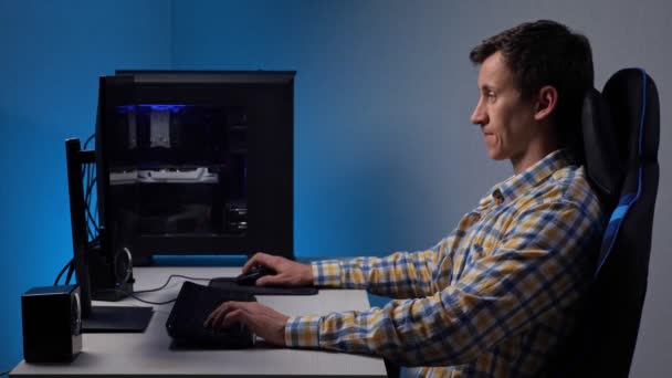 男は、モニターによって照らされた半暗い部屋でゲームチェアに座って大規模なコンピュータ画面上でビデオゲームをプレイ. — ストック動画