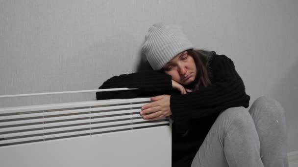 Mladá žena chytí rýmu a sedí v blízkosti ohřívače oblečený teple — Stock video