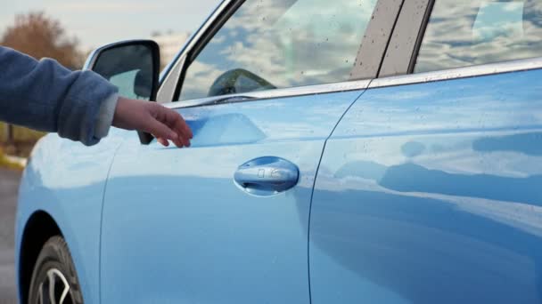 Женщина-водитель садится в синий иностранный автомобиль на осенней улице — стоковое видео
