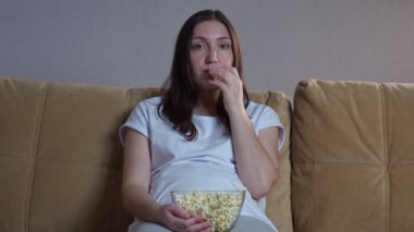Gözlüklü kadın patlamış mısır yiyor ve televizyon izliyor.