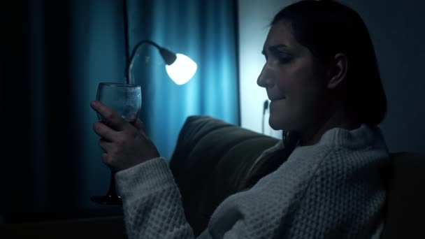 Przygnębiona kobieta pije alkohol w ciemności salonu — Wideo stockowe