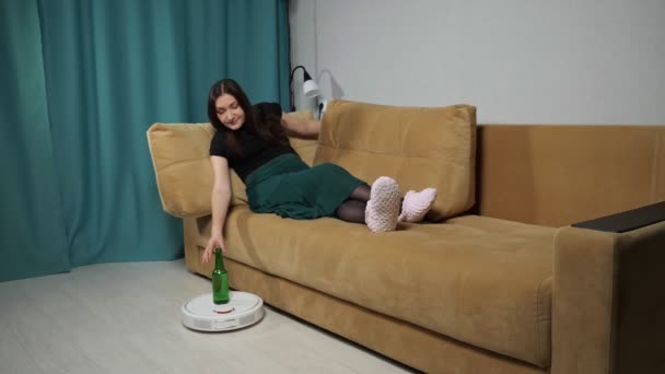 Робот-пилосос доставляє алкоголь жінці, що сидить на дивані — стокове відео