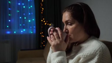Esmer kadın Noel 'de kanepede oturup sıcak kahve içer.
