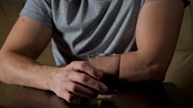 Adam oturma odasındaki kanepede oturup viski içiyor.
