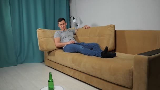Robot aspiradora entrega alcohol al hombre sentado en el sofá — Vídeos de Stock