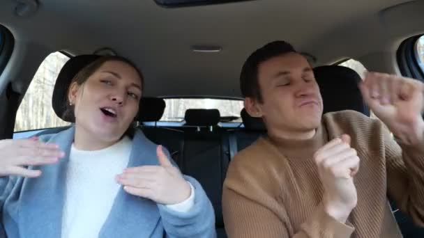 Dark-haired man in sweater and brunette woman in shirt and coat sing and dance listening to loud music sitting in car cabin. — Stock Video
