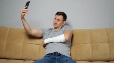 Genç adam kırık koluyla poz vererek selfie çekiyor.