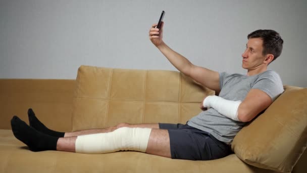 Mladý muž se zraněným kolenem a předloktím bere selfie — Stock video