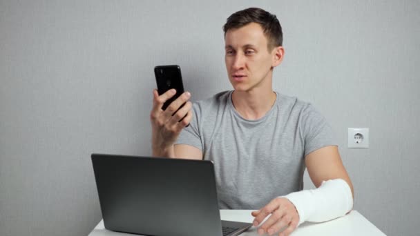 Hombre con el brazo roto trabaja hablando a través de videollamada — Vídeos de Stock