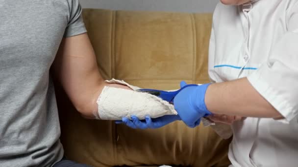 Νοσοκόμα κόβει γύψο επίδεσμο από θεραπευμένο χέρι του νεαρού άνδρα — Αρχείο Βίντεο