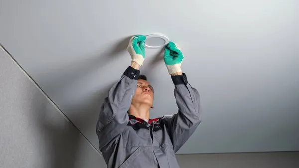 Electrician installs light on ceiling at flat renovation — Stock Photo, Image