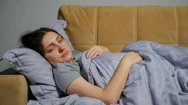 Хвора молода жінка лежить на дивані під ковдрою і кашляє — стокове фото