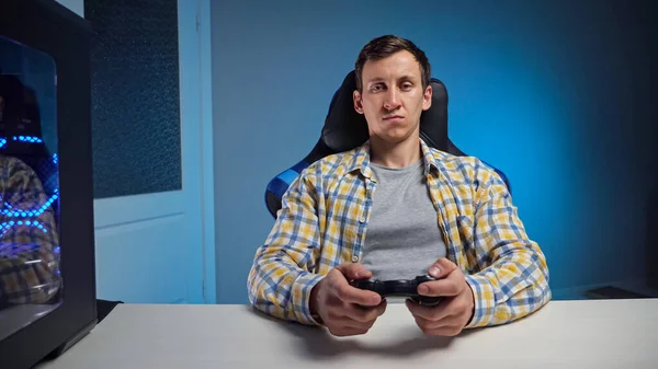 Junger Mann spielt Computerspiel mit Gamepad im halbdunklen Raum — Stockfoto