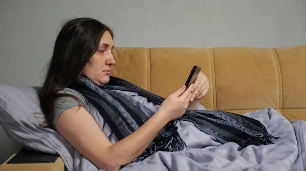 Sick woman sits on sofa and orders medicine via smartphone — Stock Photo, Image
