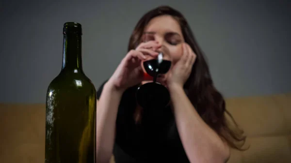暗いです緑のアルコールボトルに対してぼやけたブルネットとともに落ち込んで顔式ドリンクワインのワイングラス — ストック写真