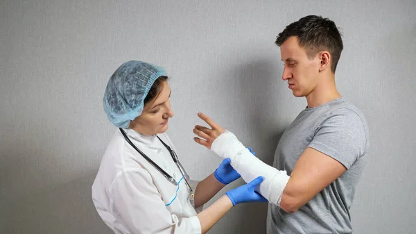 Médico morena examina el antebrazo roto del joven — Foto de Stock