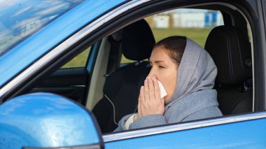 Woman sneezes and blows nose in paper napkin sitting in car clipart