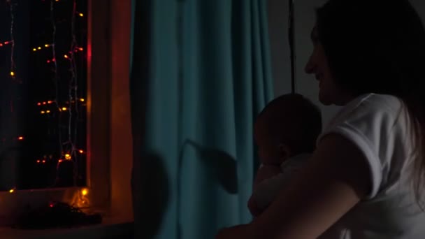 Brunette moeder houdt in armen baby jongen op slinger op venster — Stockvideo