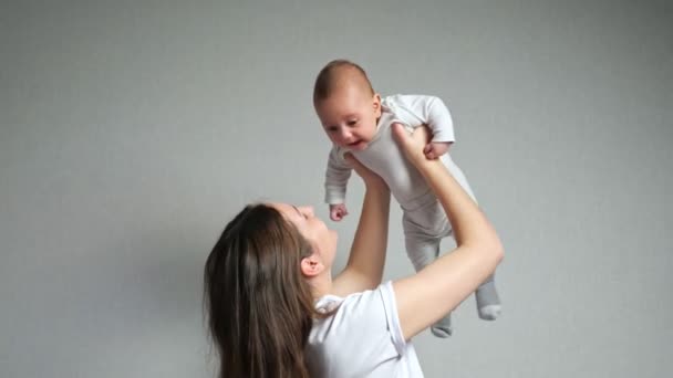 Young mother plays with love with baby against grey wall — Stock Video