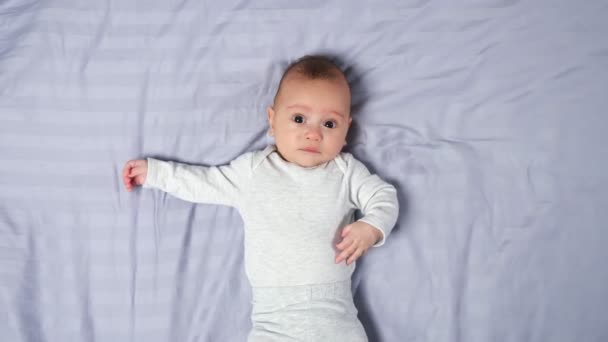 Baby boy lies on blanket and moves looking into camera — Stock Video