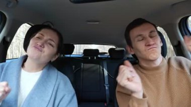 Kadın ve erkek arabada oturup müzik dinler ve dans ederler.