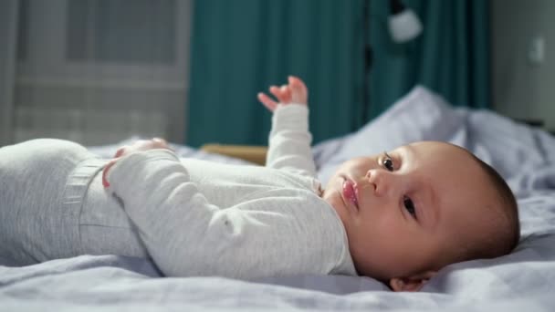 Baby pojke ligger på sängen och flyttar blåser bubblor från saliv — Stockvideo