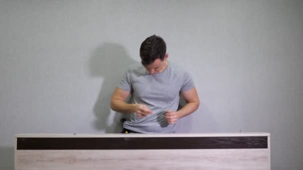 Man in a gray T-shirt assembles furniture using a screwdriver — Stock Video