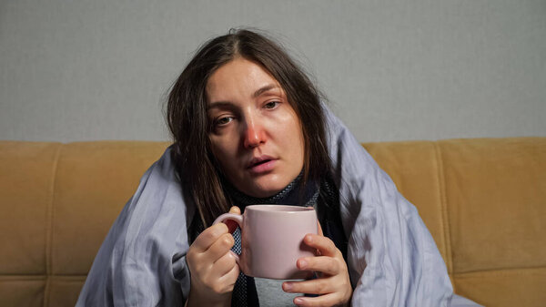 Woman falls ill and drinks tea wrapped in blanket on sofa