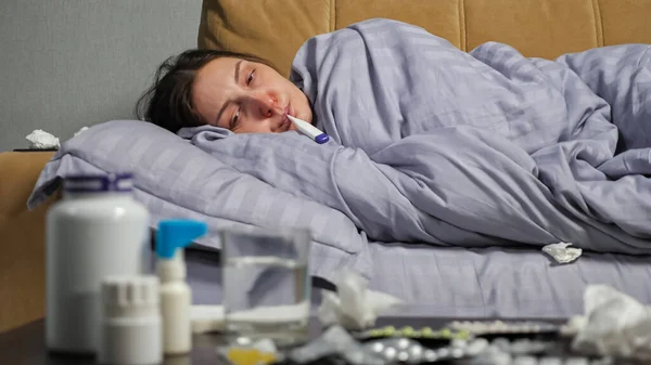 Mujer enferma mide la temperatura acostada en el sofá — Foto de Stock
