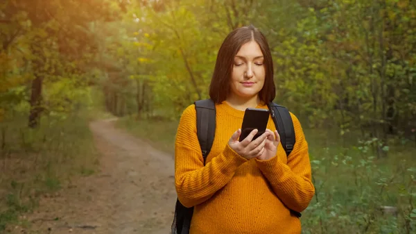 Női túrázó üzenetek mobiltelefon álló zöld erdő — Stock Fotó