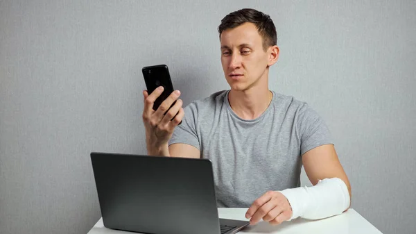 Hombre con el brazo roto trabaja hablando a través de videollamada —  Fotos de Stock