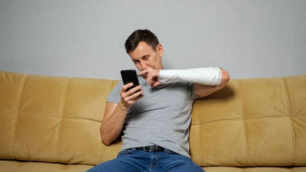 Hombre morena escoge la nariz con el brazo roto desplazándose por las redes sociales — Foto de Stock