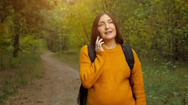 Улыбающаяся путешественница разговаривает на смартфоне в осеннем лесу — стоковое фото